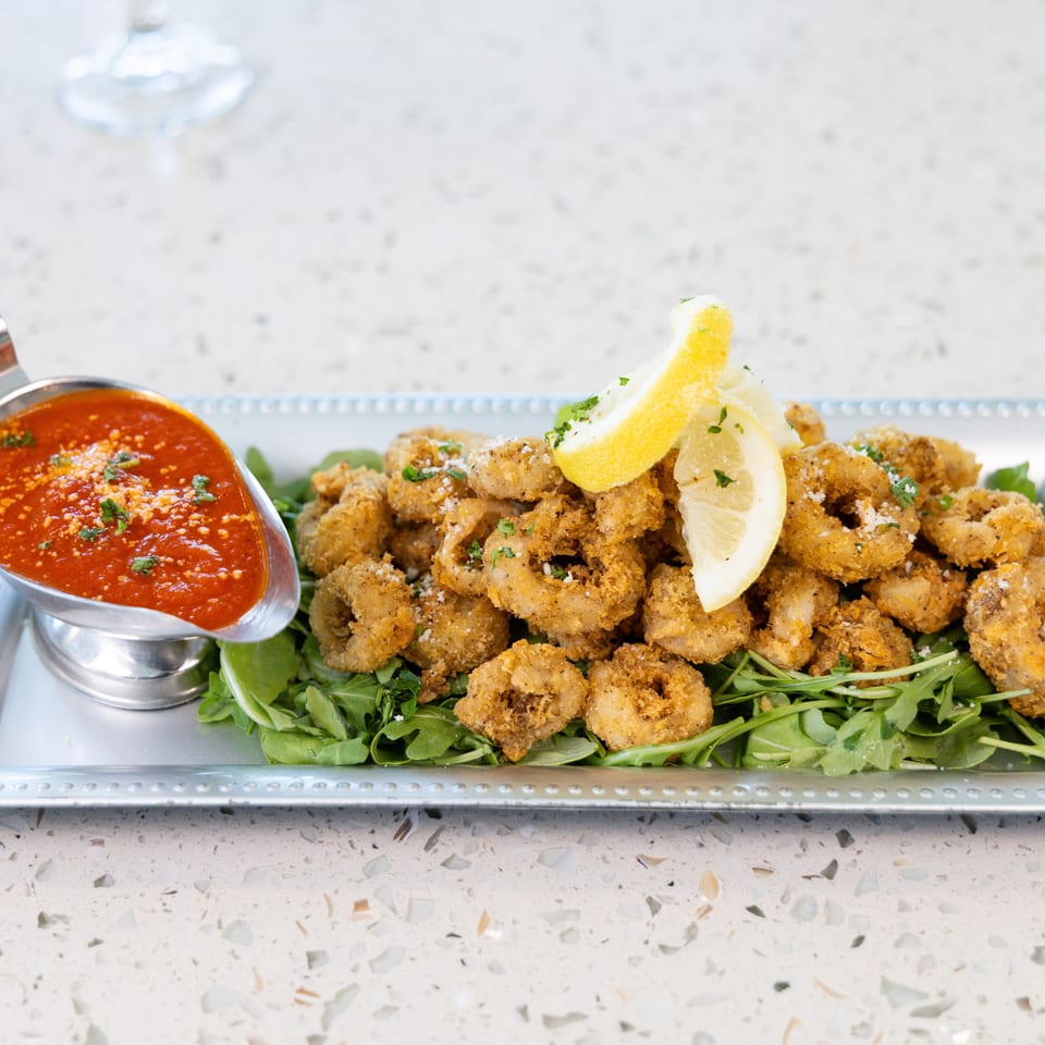 Crispy fried calamari rings with lemon wedges and marinara sauce on a bed of arugula.