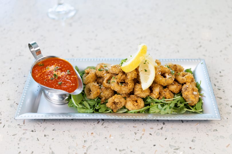 Crispy fried calamari rings with lemon wedges and marinara sauce on a bed of arugula.