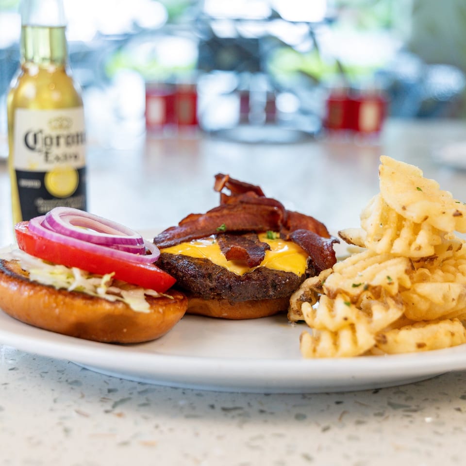 A bacon cheeseburger with waffle fries and a Corona beer bottle on a white plate.