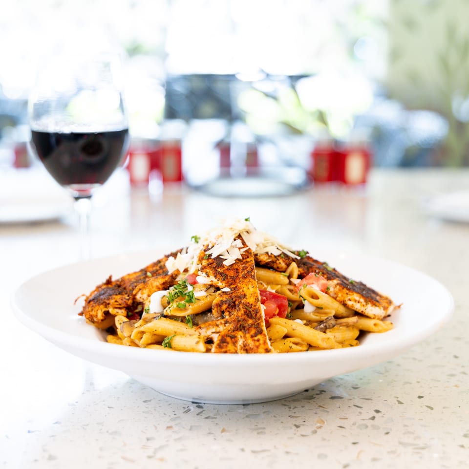 Blackened chicken pasta with penne, tomatoes, mushrooms, and parmesan, with a glass of red wine.