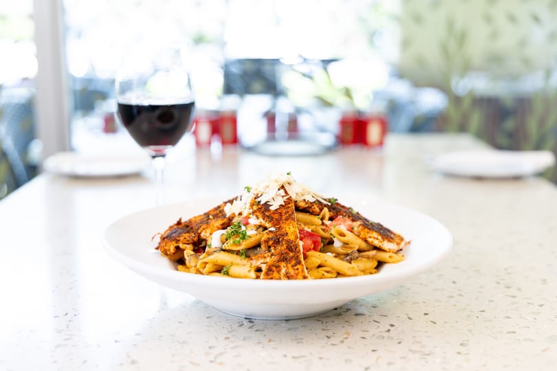 Blackened chicken pasta with penne, tomatoes, mushrooms, and parmesan, with a glass of red wine.