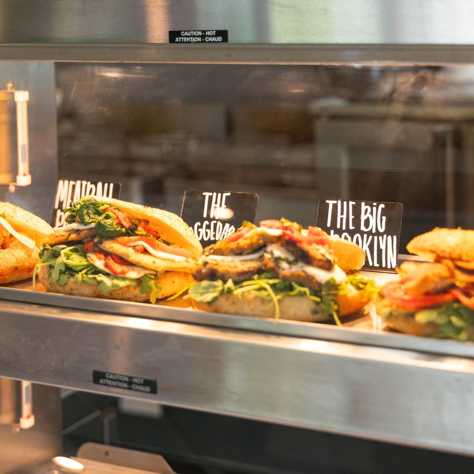 Assortment of gourmet sandwiches, including a meatball sub, displayed in a heated glass case.