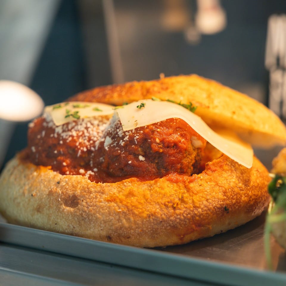 Meatball sub with marinara sauce, parmesan, and a slice of cheese on a golden bun.