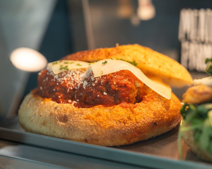 Meatball sub with marinara sauce, parmesan, and a slice of cheese on a golden bun.