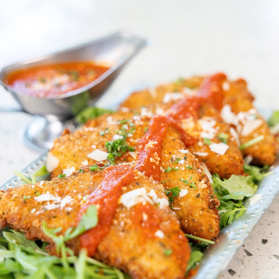 Golden-fried mozzarella triangles topped with marinara sauce, parmesan, and parsley on a bed of arugula.