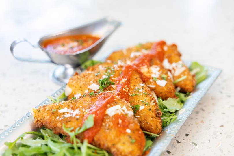Golden-fried mozzarella triangles topped with marinara sauce, parmesan, and parsley on a bed of arugula.