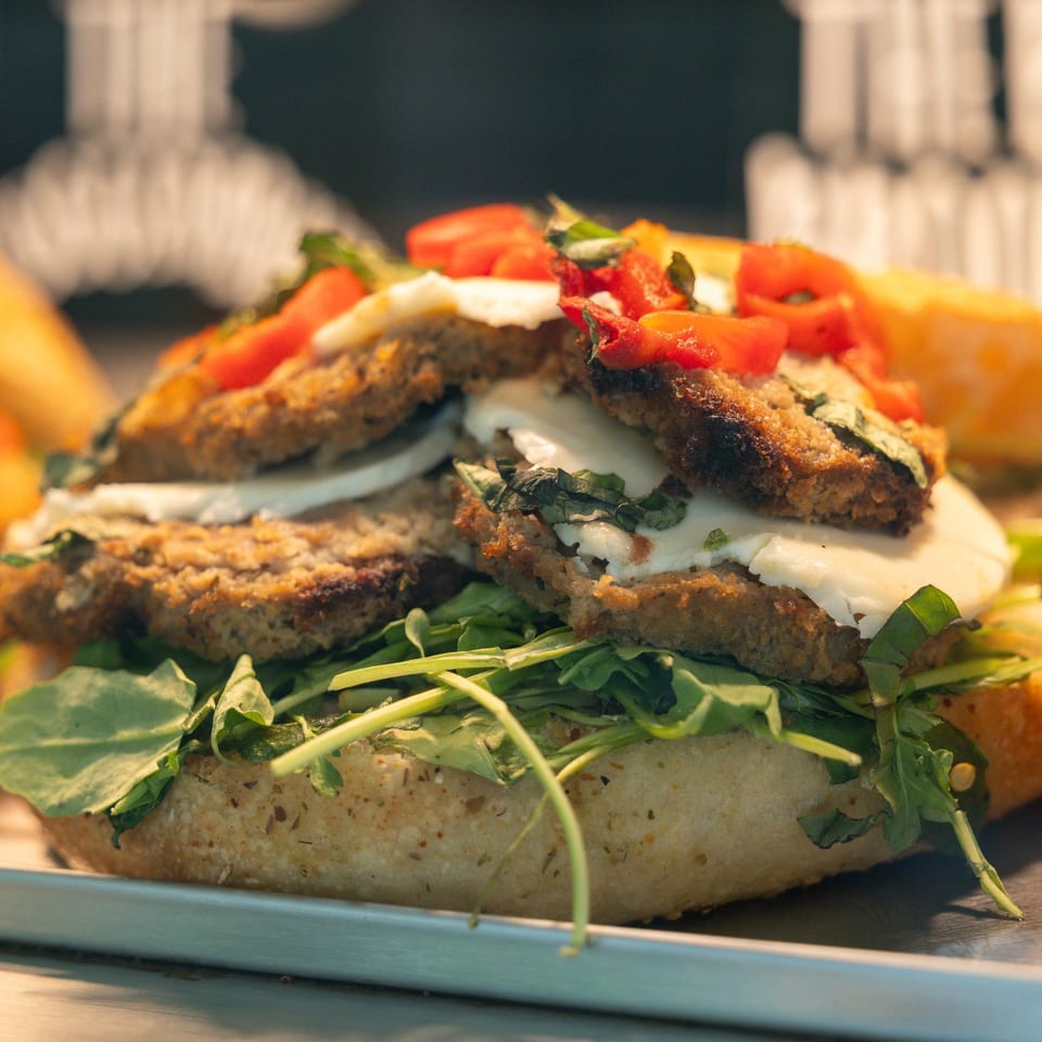 Close-up of a sandwich with breaded cutlets, fresh mozzarella, arugula, and diced tomatoes.