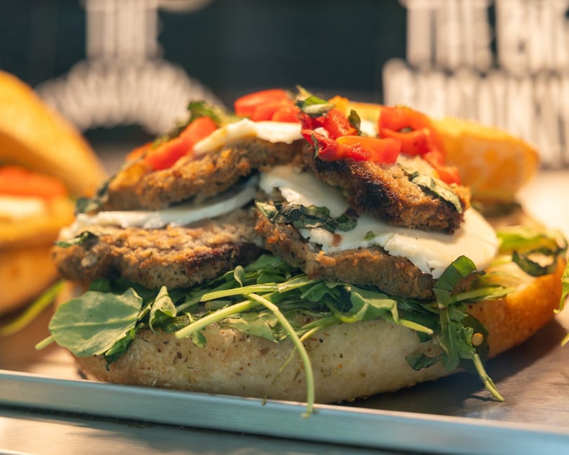 Close-up of a sandwich with breaded cutlets, fresh mozzarella, arugula, and diced tomatoes.