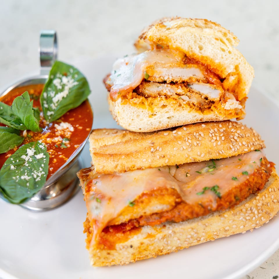Chicken parmesan sandwich with melted cheese and red sauce, served with a side of marinara.