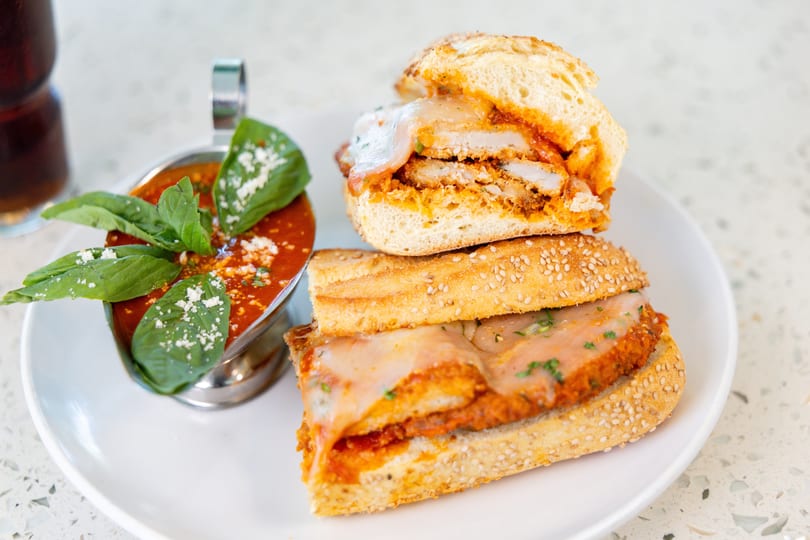 Chicken parmesan sandwich with melted cheese and red sauce, served with a side of marinara.