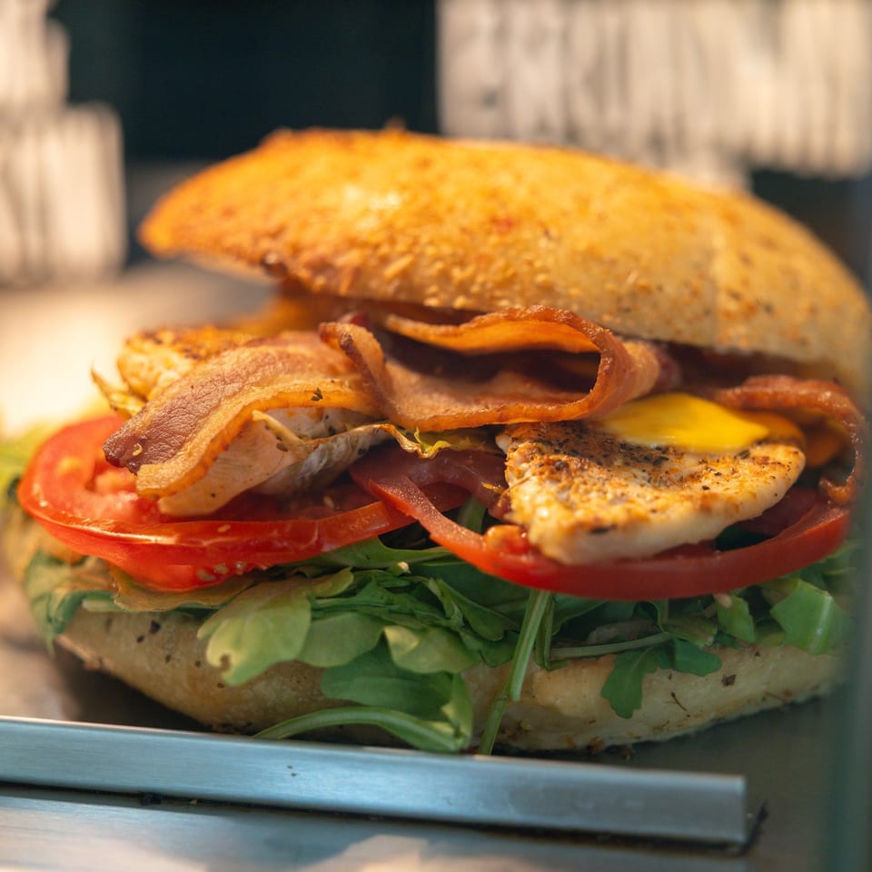 Close-up of a chicken and bacon sandwich with tomato, arugula, and cheese on a bun.