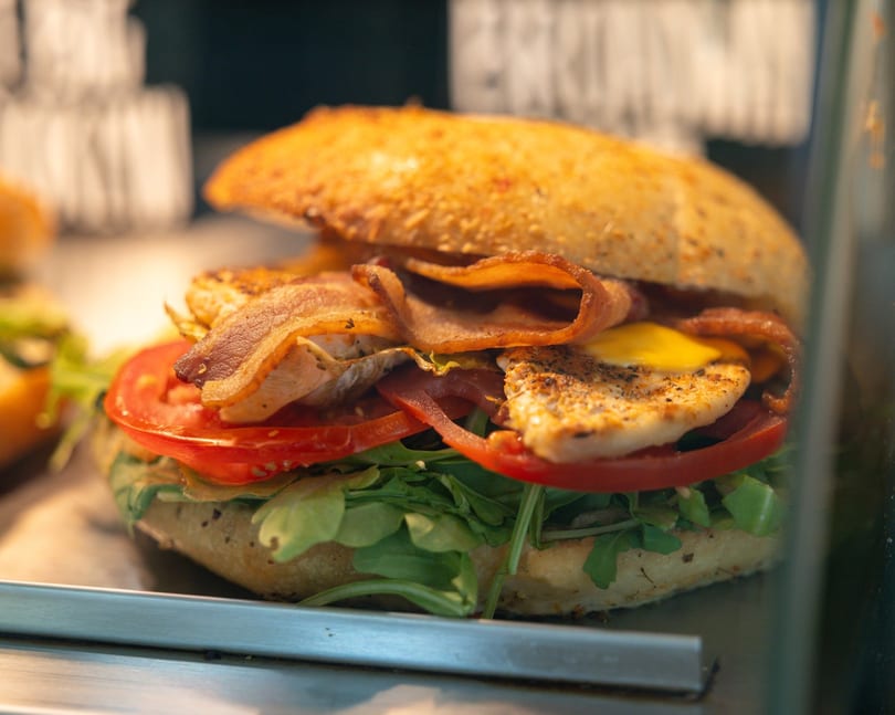 Close-up of a chicken and bacon sandwich with tomato, arugula, and cheese on a bun.