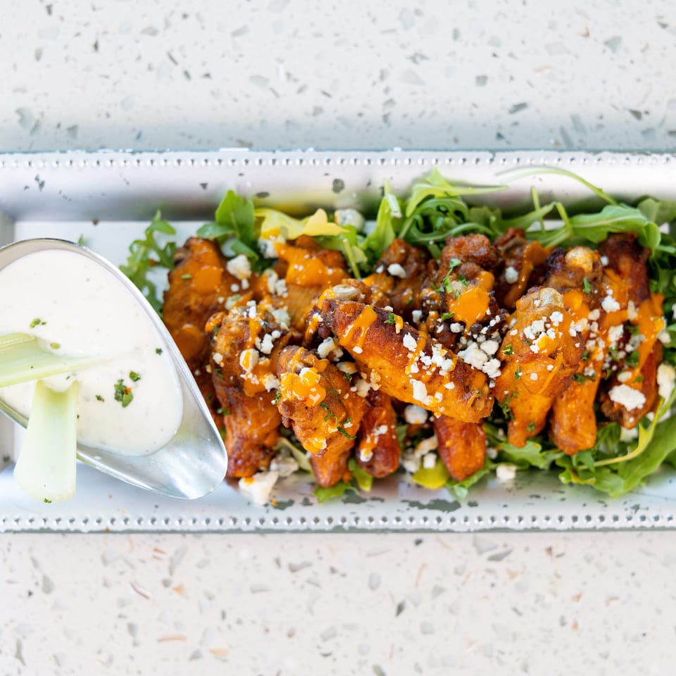 Buffalo wings with blue cheese crumbles and ranch dressing on a bed of arugula.