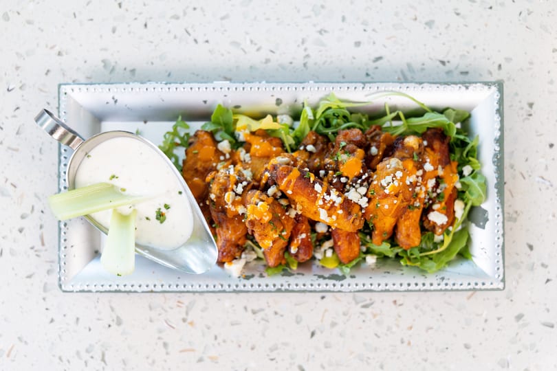 Buffalo wings with blue cheese crumbles and ranch dressing on a bed of arugula.