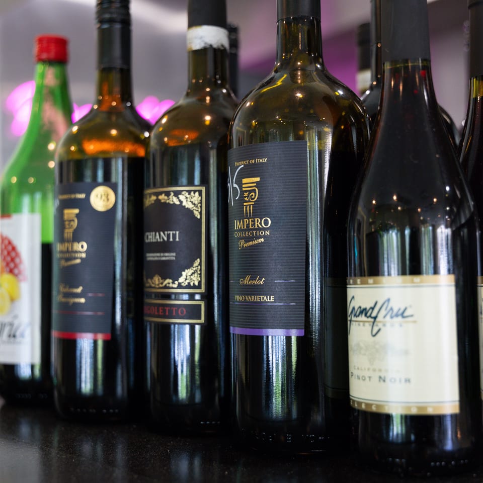 A close-up of several dark wine bottles with various labels, including "Impero" and "Chianti".