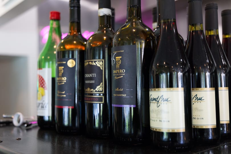 A close-up of several dark wine bottles with various labels, including "Impero" and "Chianti".